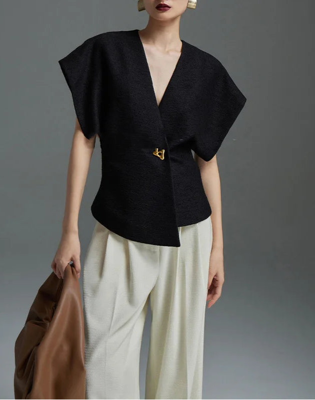 Person wearing a black top and white pants holding a brown bag against a gray background