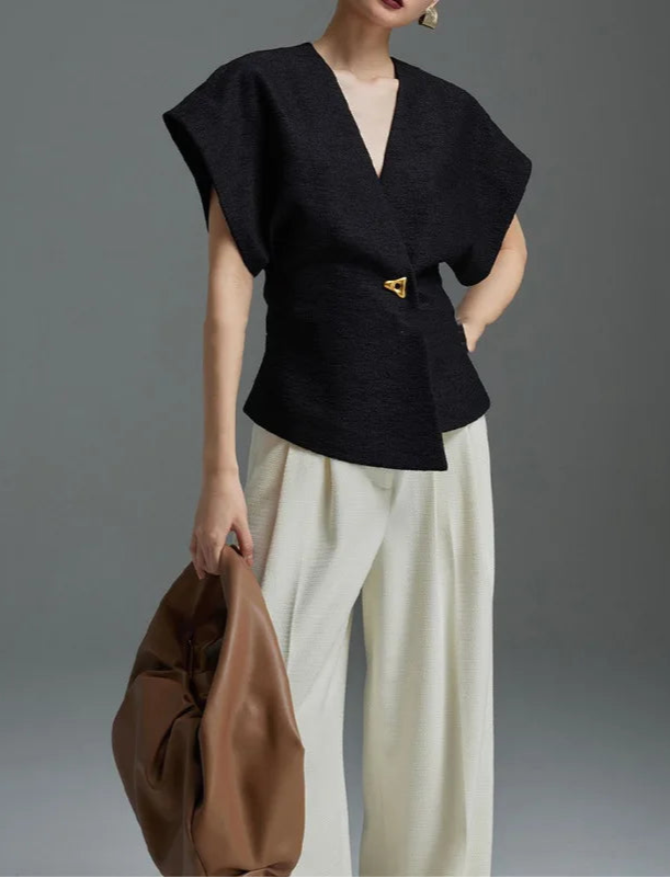 Person wearing a black top and white pants holding a brown bag against a gray background