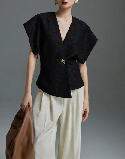 Person wearing a black top and white pants holding a brown bag against a gray background