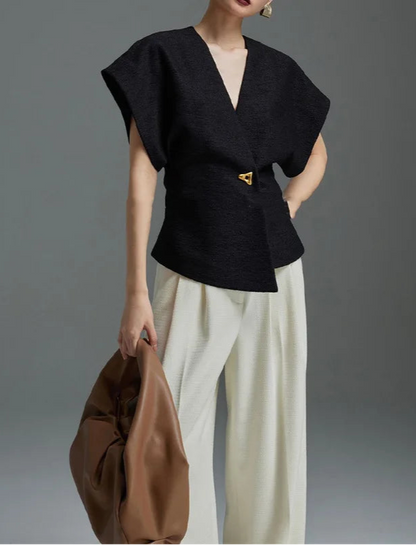 Person wearing a black top and white pants holding a brown bag against a gray background